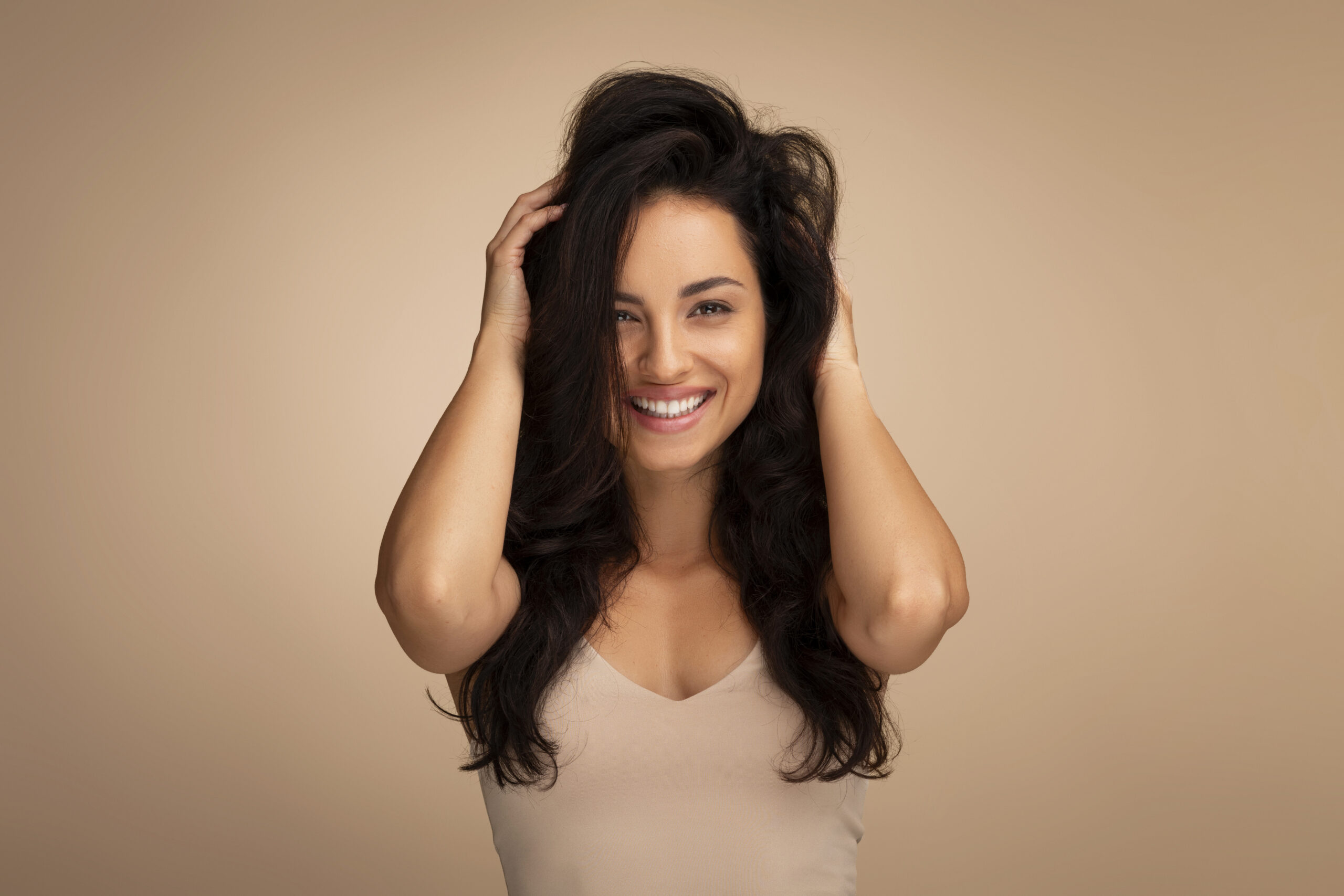 Hair Care And Therapy Treatment Concept. Portrait of smiling hispanic woman posing and holding dark long hair. Beautiful millennial lady standing isolated over beige studio background, copy space