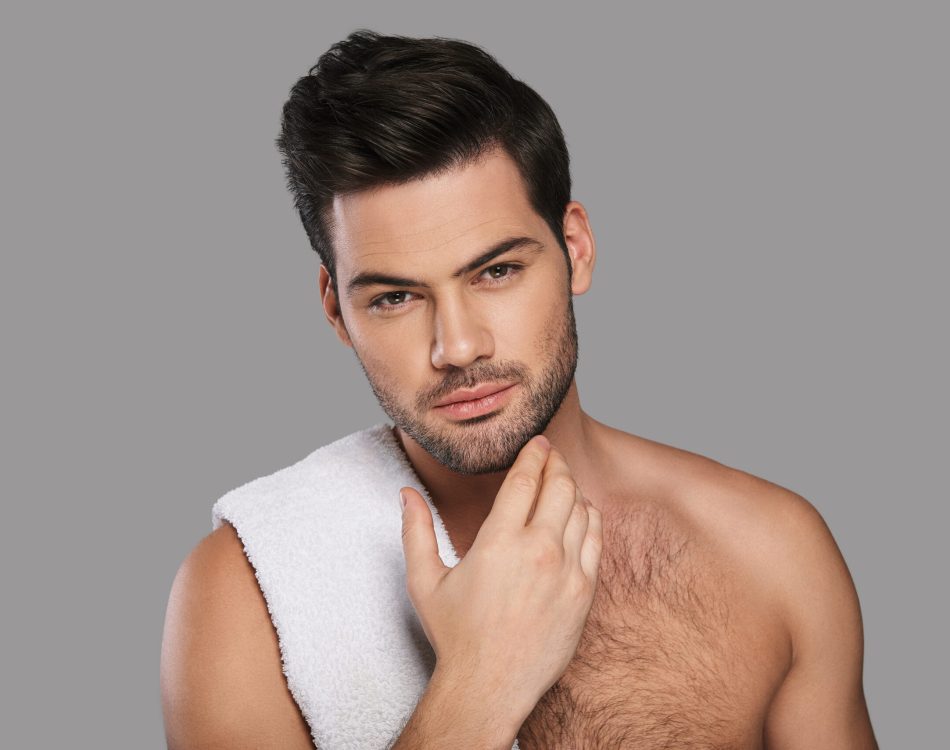 He is looking right into your heart. Handsome young man looking at camera and keeping hand on chin while standing against grey background